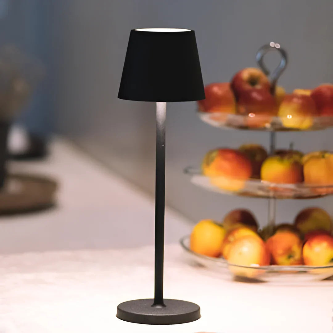 A cordless black table lamp stands prominently beside a tiered fruit stand filled with colorful apples, illuminating the space beautifully.