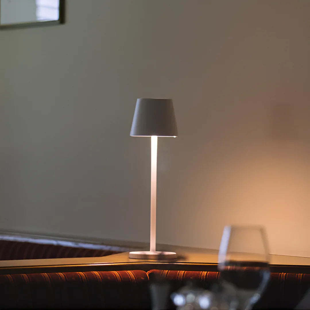 A wireless modern table lamp with a sleek design casts soft light on a wooden surface, creating a warm, inviting ambiance.