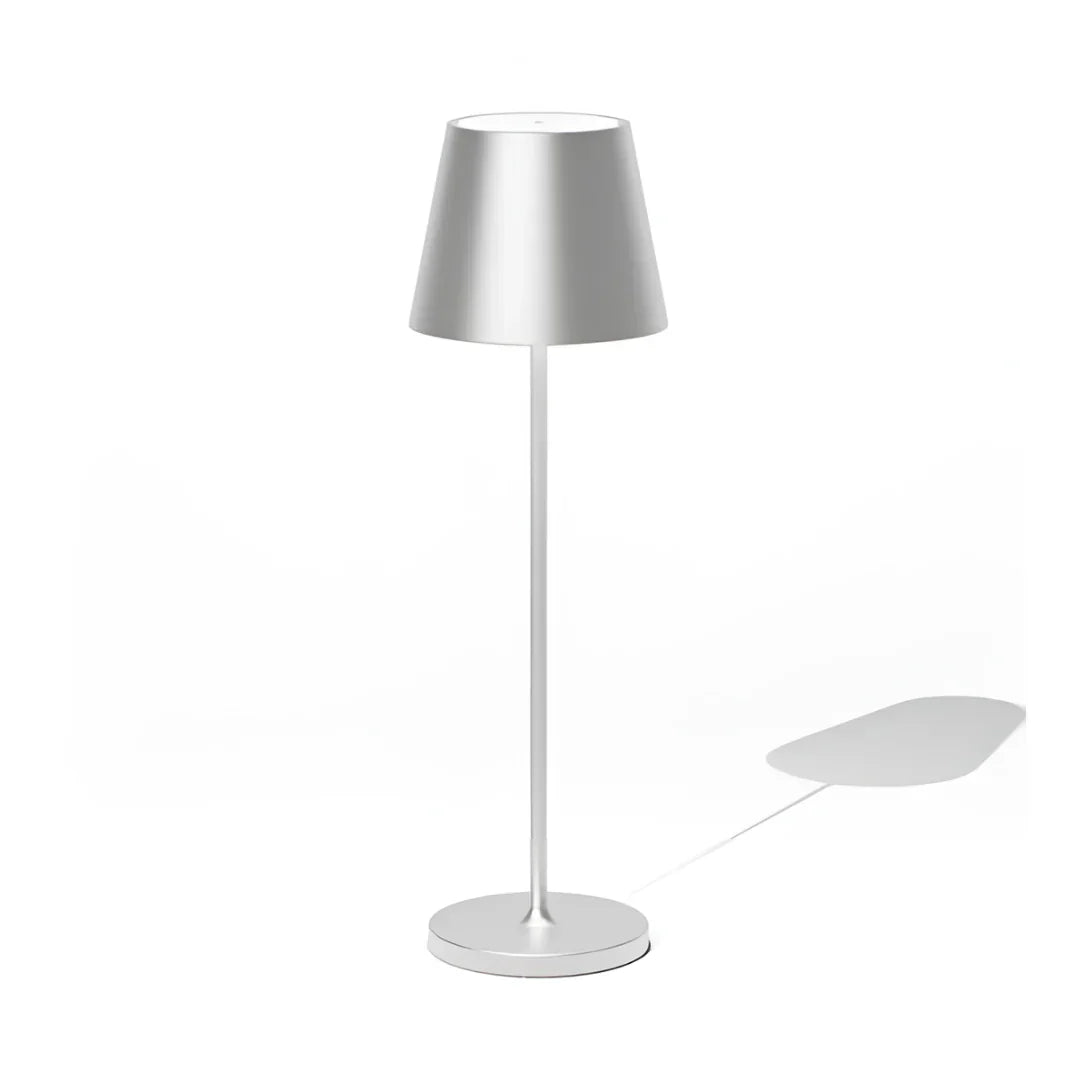 Modern wireless silver table lamp with a conical shade, standing on a circular base, casting a subtle shadow on a white background.