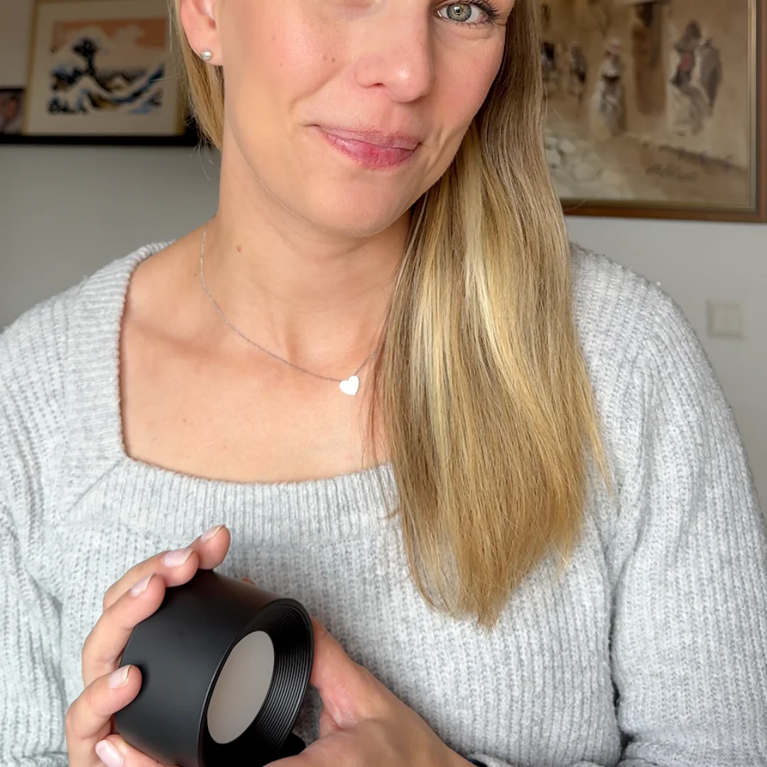 Woman holding a black wall lamp indoors with framed pictures on the wall.