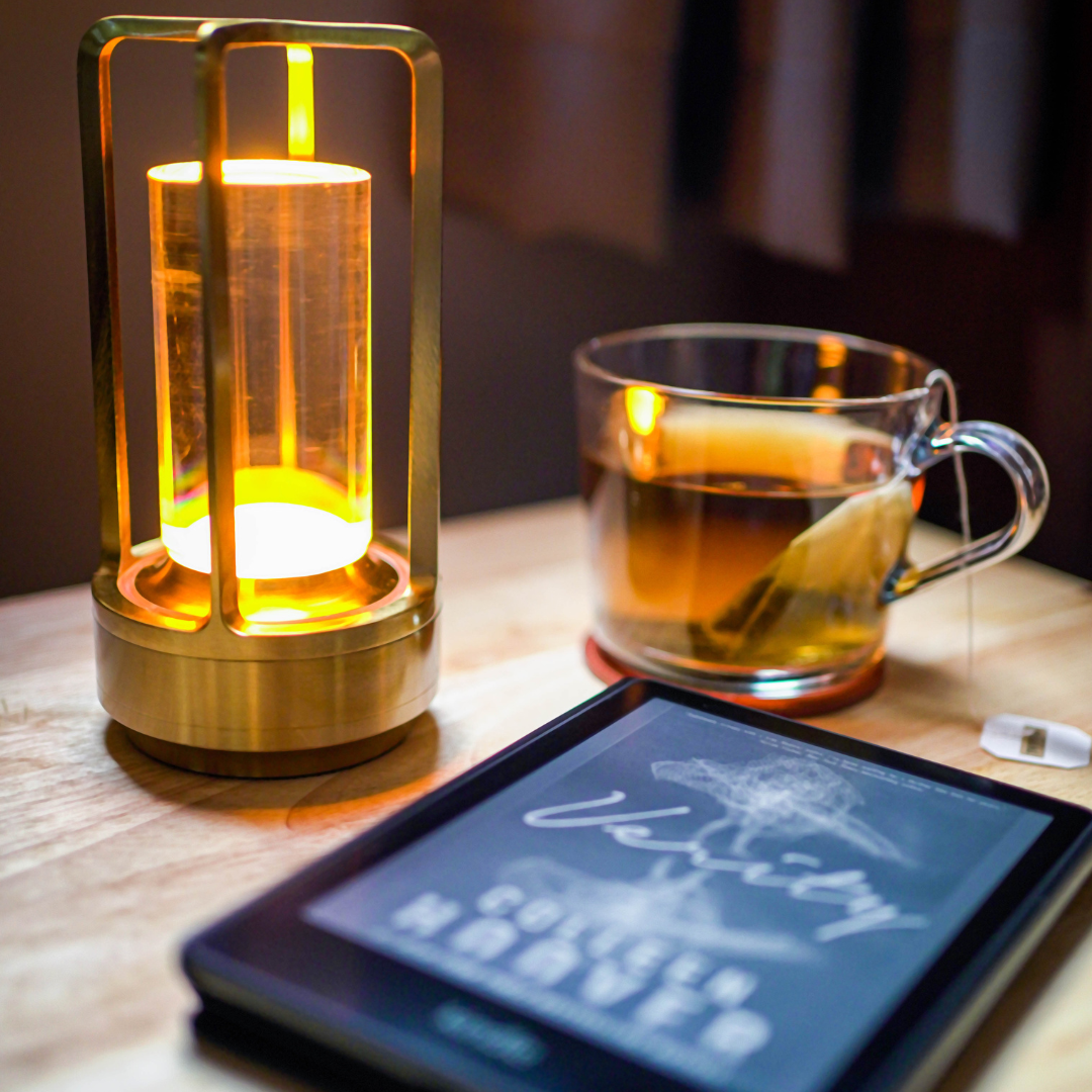 A cozy scene featuring a glowing lamp, a steaming cup of tea, and an e-reader displaying "Verity" by Colleen Hoover on a wooden table.