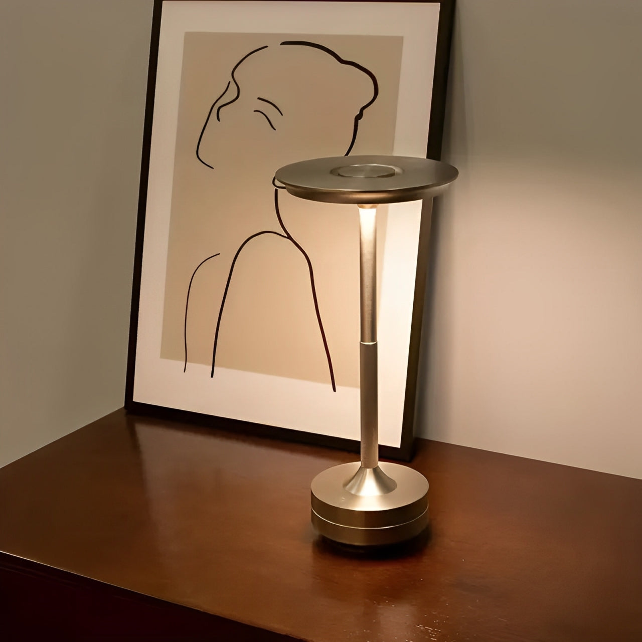 A sleek, modern lamp illuminates a minimalist line drawing of a woman's profile, set on a wooden table against a neutral wall.