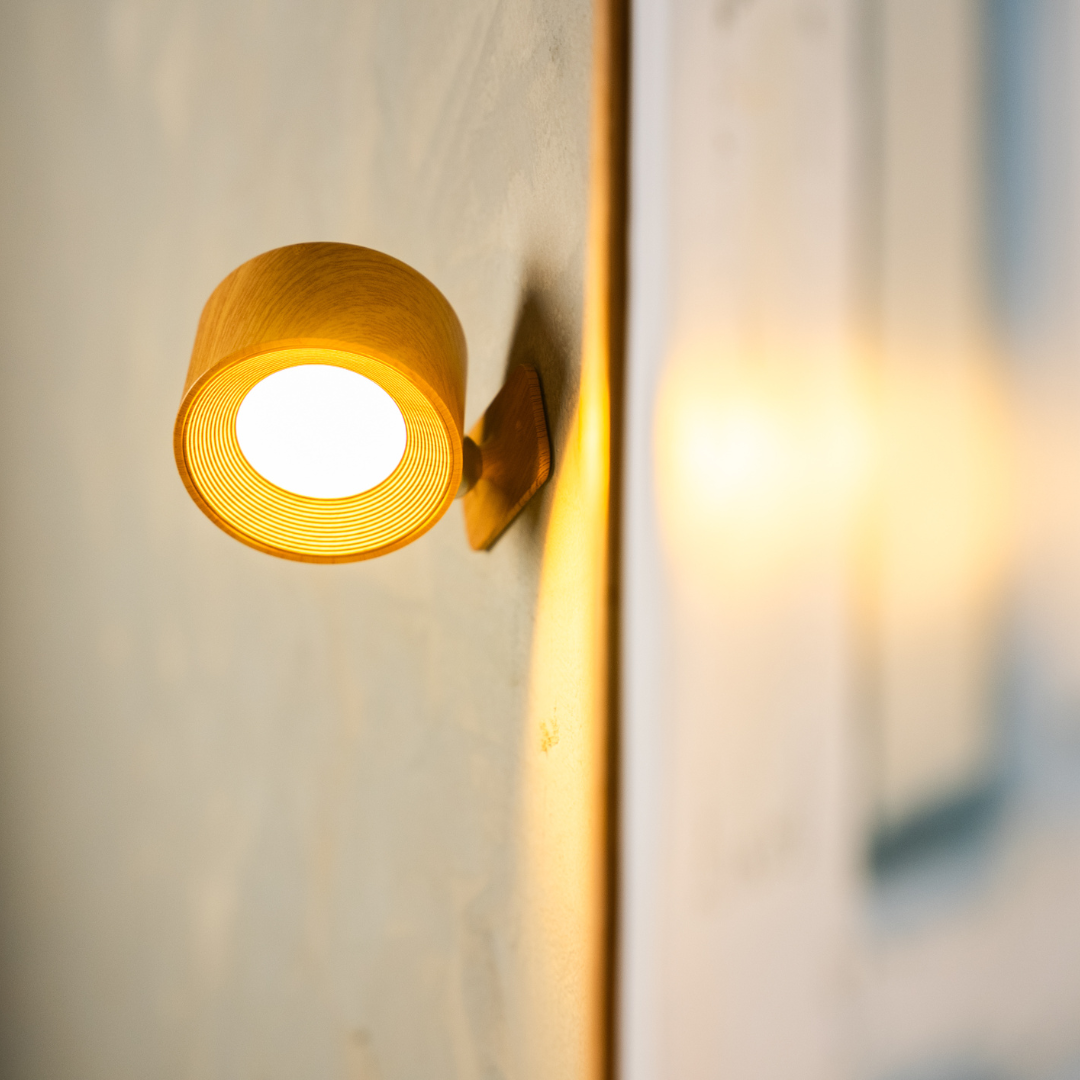 Warm wooden wall lamp with a circular design, mounted on a textured wall, illuminating the space softly.