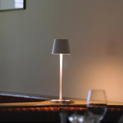 A wireless modern table lamp with a sleek design casts soft light on a wooden surface, creating a warm, inviting ambiance.